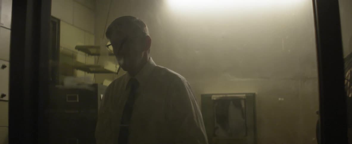 A man stands in a smoky room and puts a cigarette in his mouth
