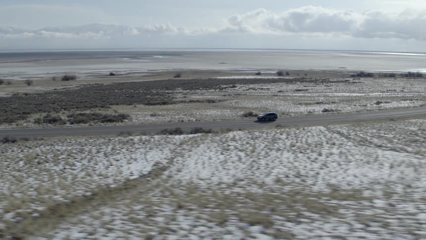 A car travels on a coastal road on a sunny winter day