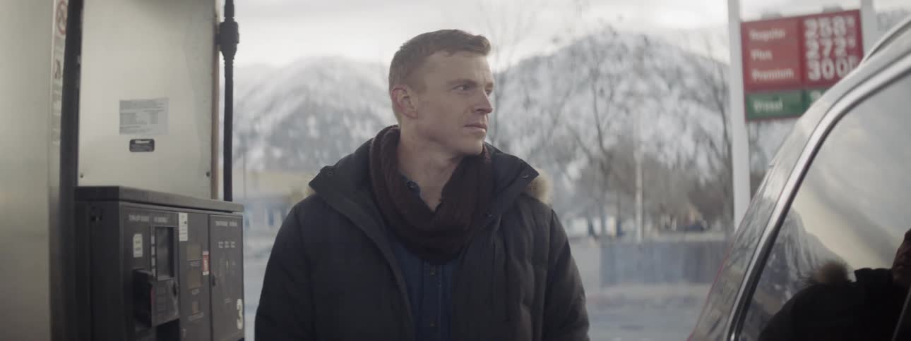 A man stands at a gas station pump on a winter day