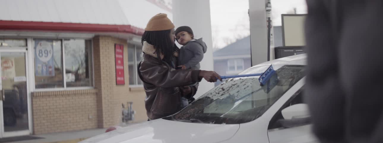 A man holds a young child as he washes a car windshield