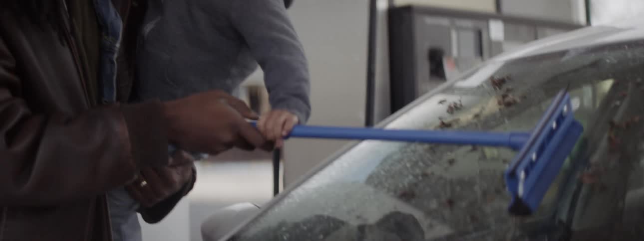 A man holds a baby while cleaning his windshield at a gas station