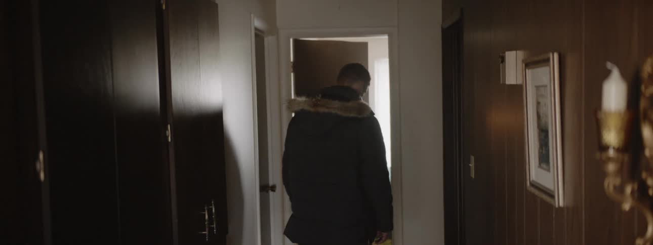 A man walks in a hallway and enters a bedroom