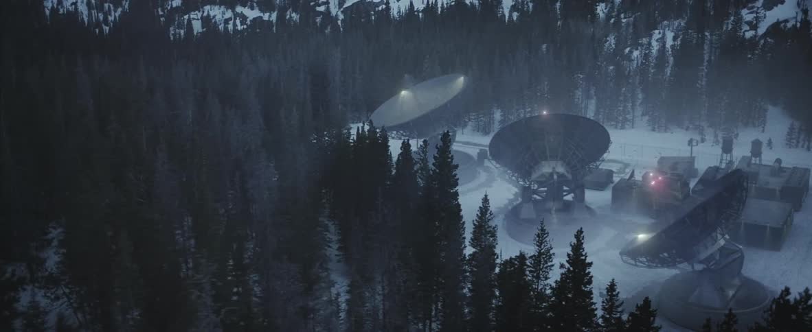 Large satellites and a small building sit in the middle of a large snowy forest