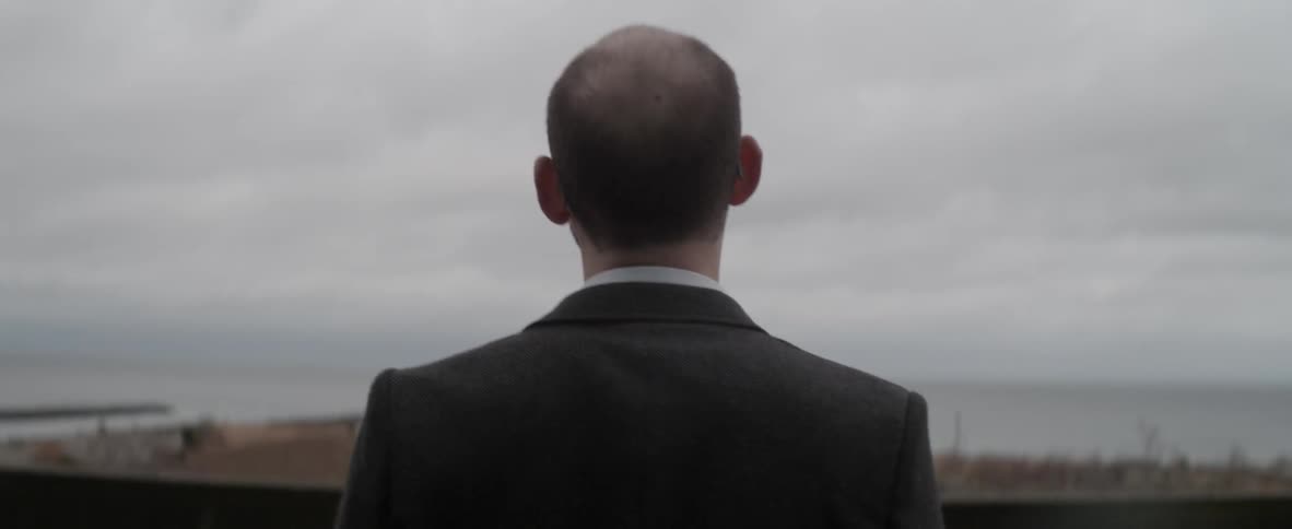 A man in a dark suit looks up at a cloudy sky