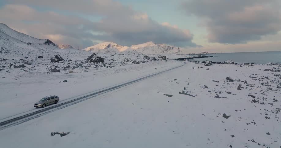 Car drives past snow covered rocks and water