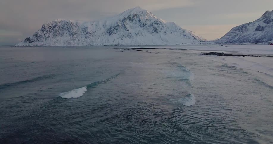 Waves wash ashore a snowy coastline at sunset