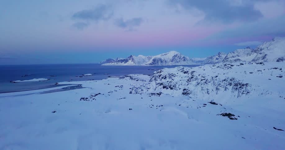 A person walks through snow and steps up onto rock to look down at the ocean