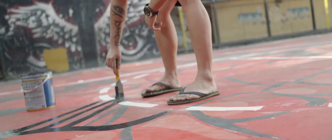 An artists is painting a mural on the ground outside in daylight