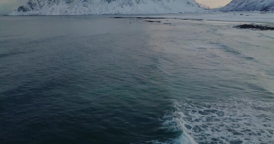 Ocean waves splash near snowy mountains