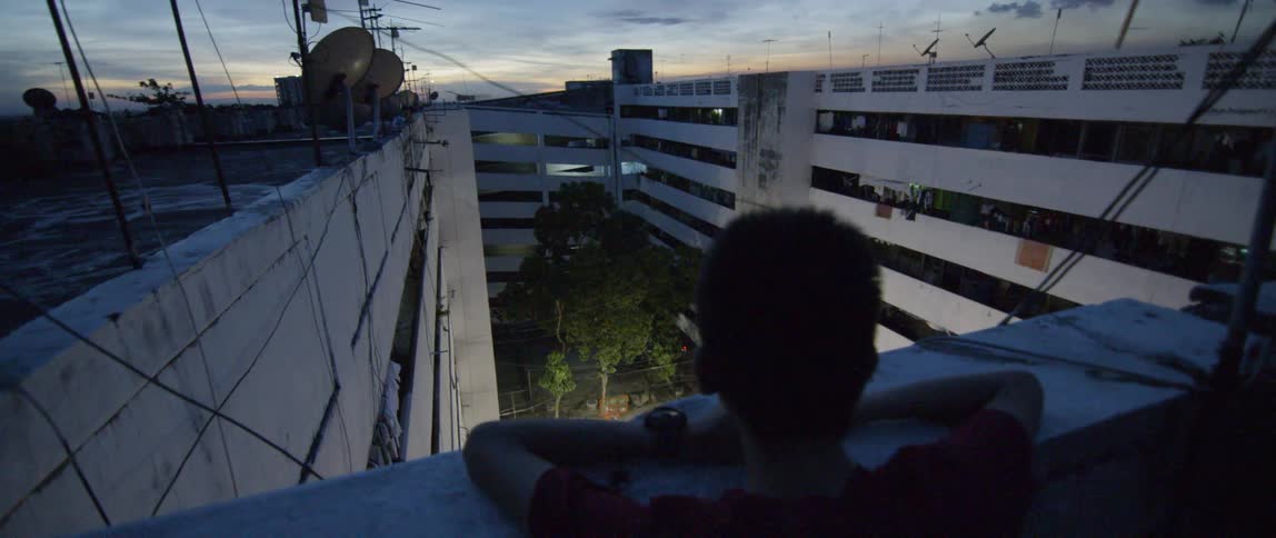 Young man leans on the ledge overlooking an outdoor basketball court