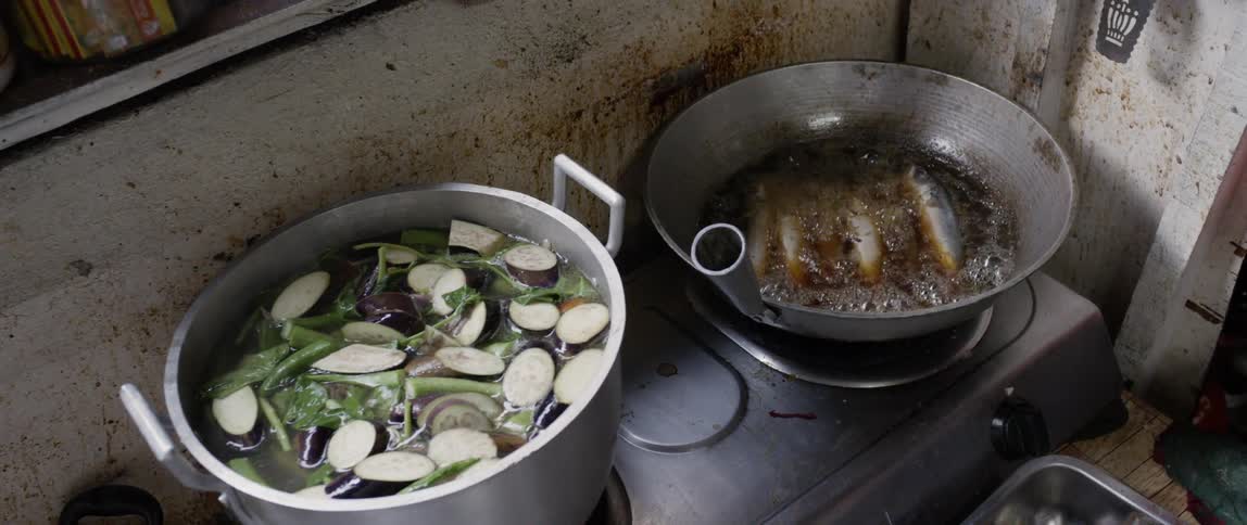 Fish boil in liquid in a pot on the stove while clams cook in a pot next to it