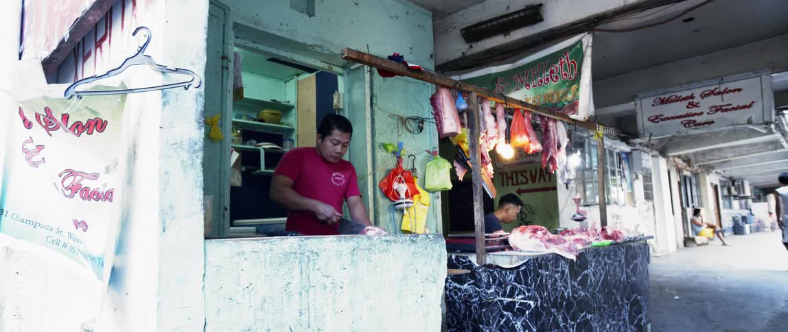 A butcher cuts and chops meat in an outdoor market