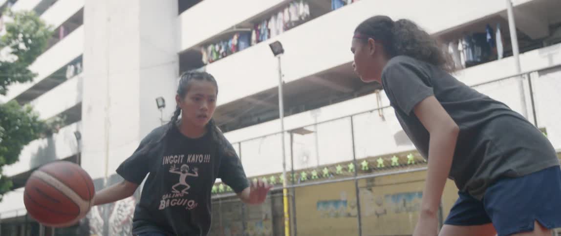 Two girls play basketball in a courtyard