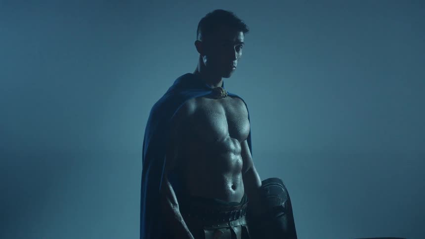 Man wearing a cape holds a sword and shield