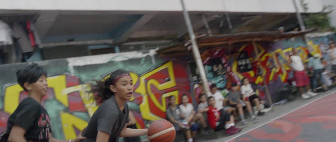 A girl goes around a defender and shoots the ball on an outdoor court