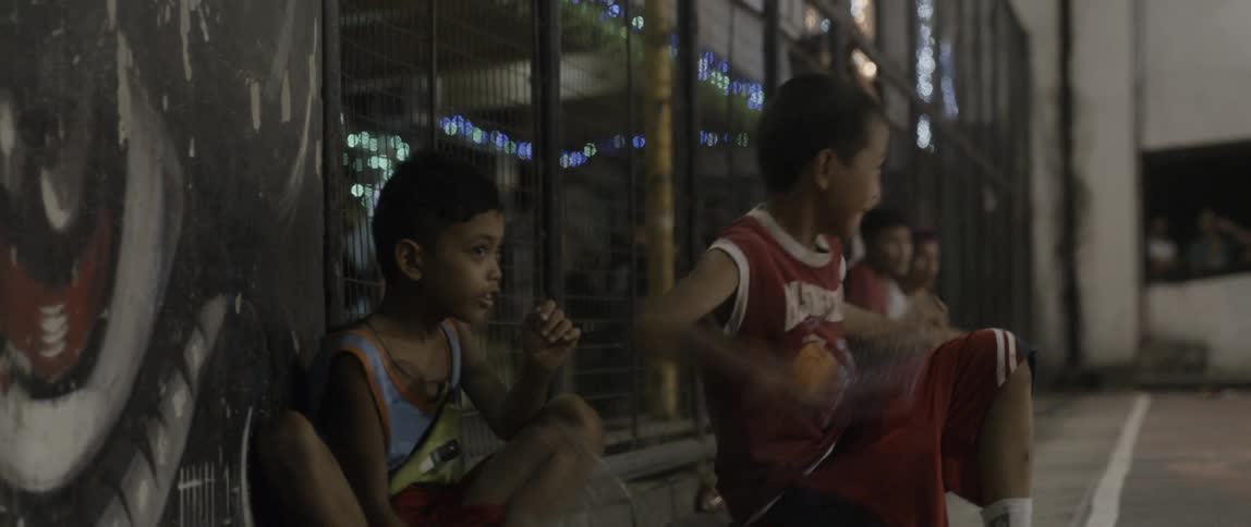 Two children kneel and  bang plastic bottles on the ground