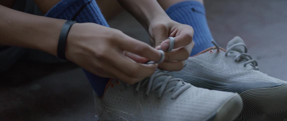 A boy is lacing up his sneakers as he sits inside on the ground in daylight