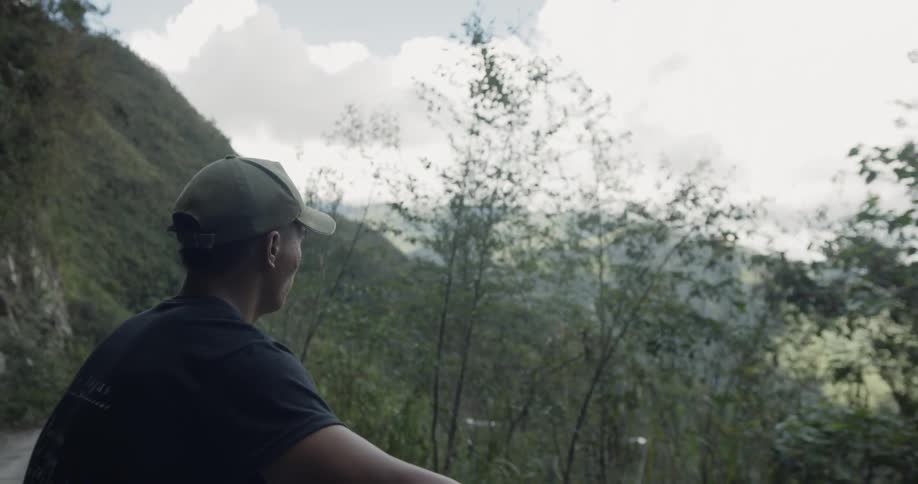 A man rides on a vehicle roof on a mountain road