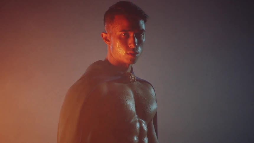 Shirtless man stands in the dark illuminated by firelight