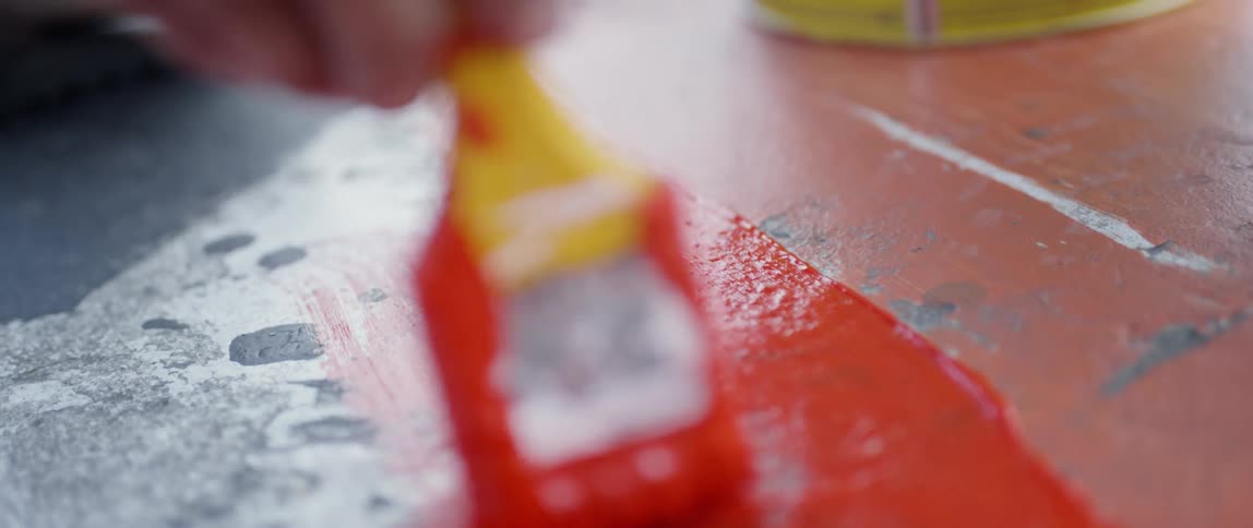 Paintbrush dipped in red paint paints a floor