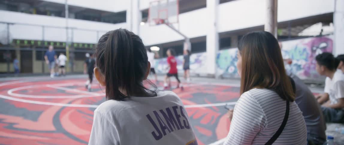 Two women sit on the sidelines of a basketball game