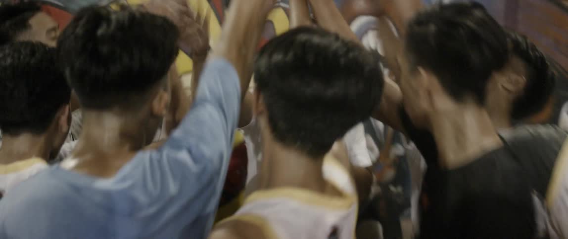 Man talking into a microphone huddles and cheers with teenagers