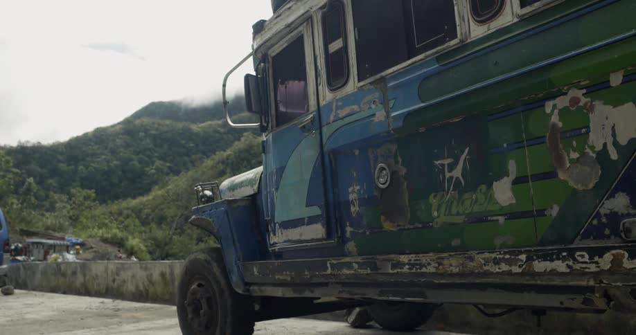 Multicolored bus parked on the side of a road near grassy hills