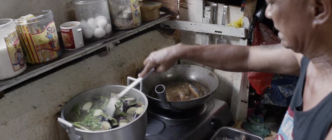 Man stirs metal pot of broiling vegetables
