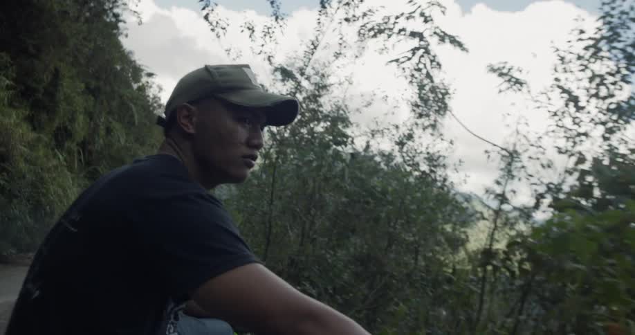 A man rides on the back of a truck on a mountain road