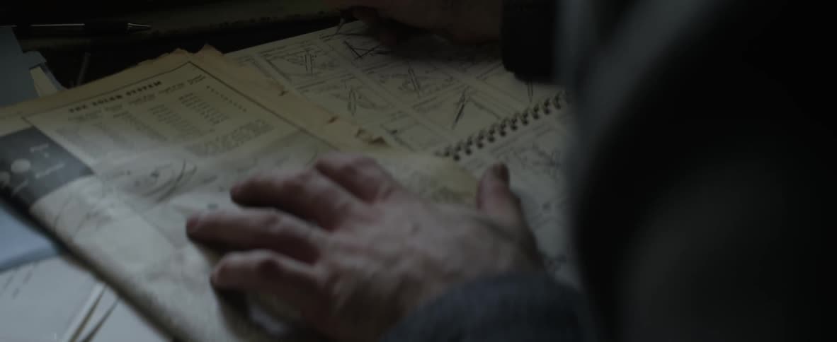 Person writing on some paper then examining a newspaper