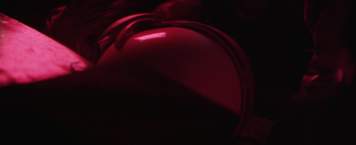 An astronaut turns and reaches for something in a red lit space