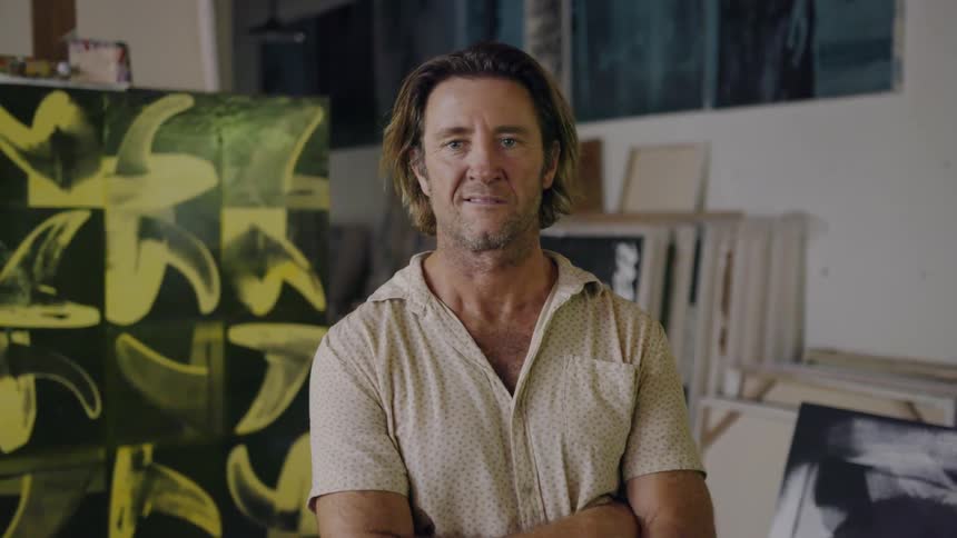 Man stands near a painting in an art studio