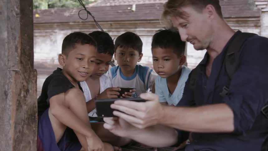 Man shows something on his cell phone screen to several young boys