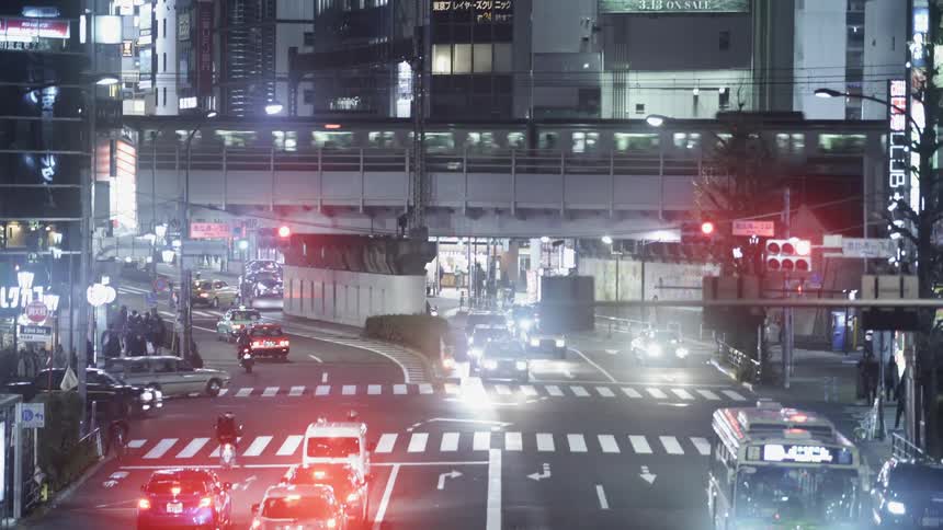 Train passes through a city at night with cars on the road underneath