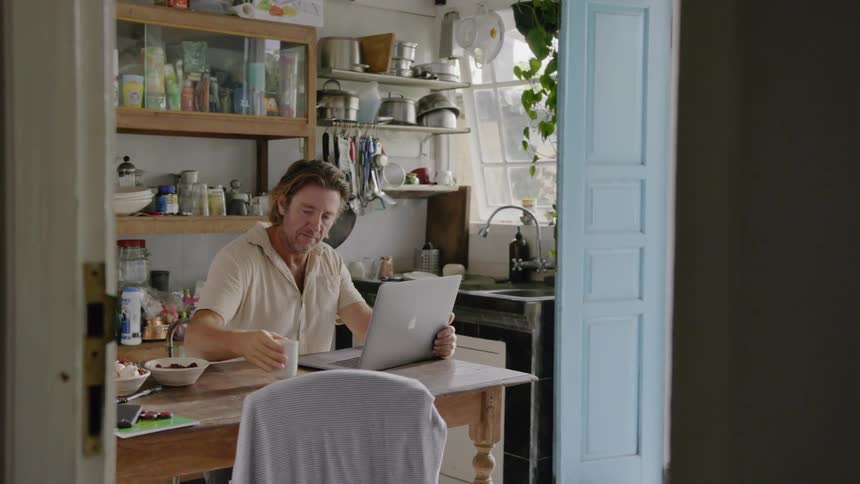 Man drinks coffee and types on a laptop in a kitchen