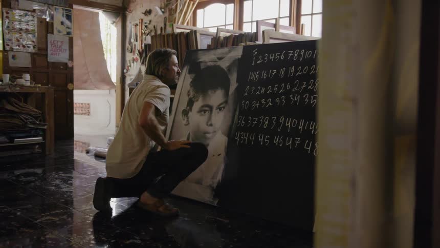 A man is admiring pictures sitting on the ground in an art studio in daylight