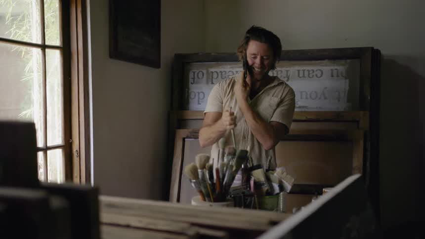 Man talks on his cellphone as he places a paintbrush into a container