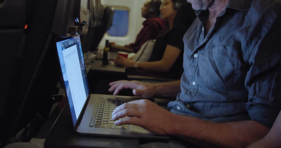Man types on a laptop while riding in an airplane