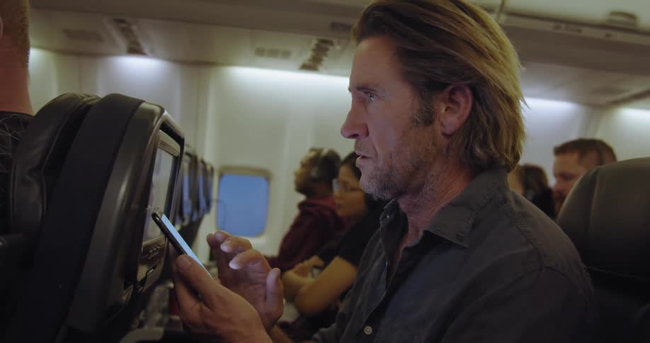 Man sits on an airplane typing on a phone