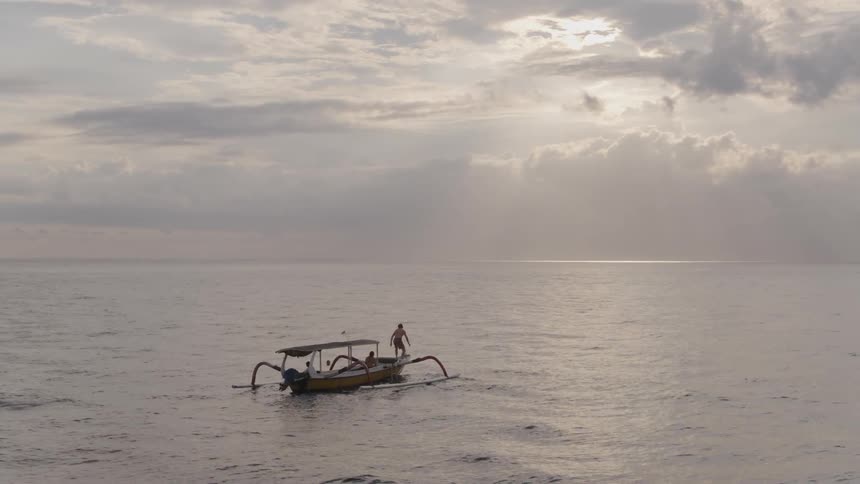A man is diving off of a boat into the ocean on a cloudy day