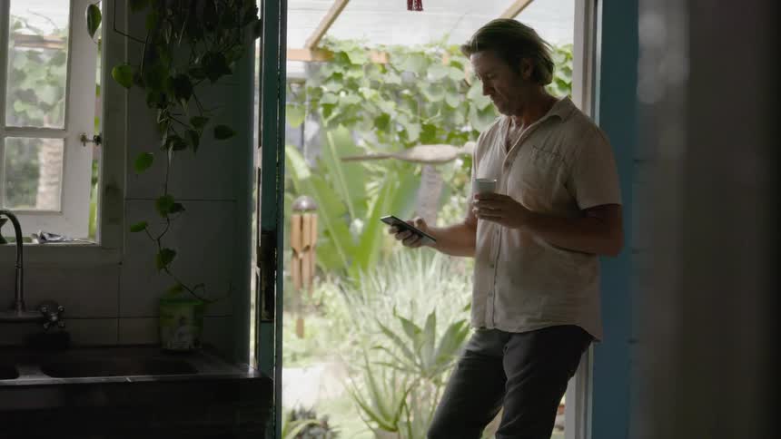 Man types on a phone while leaning in a doorway