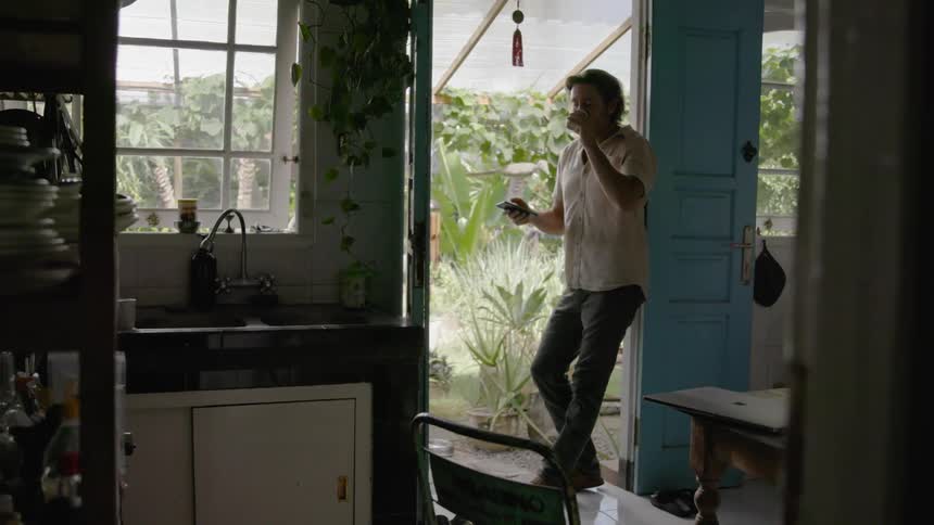 Man leans in the doorway looking at his phone and sipping from a cup