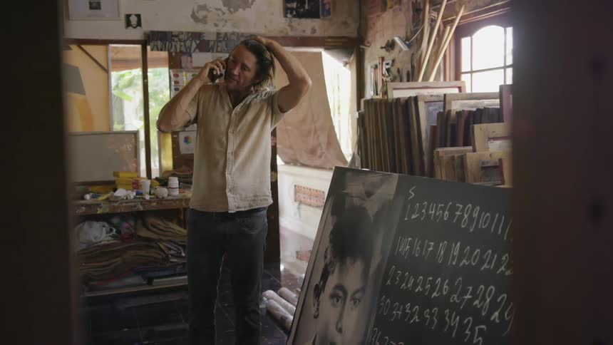 A man is standing in an art studio talking on his cellphone in daylight