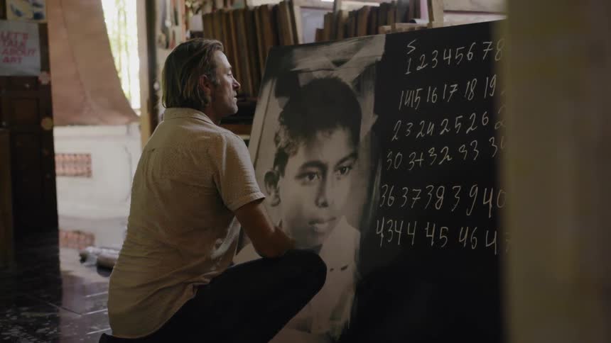 Man crouches as he looks at a painting