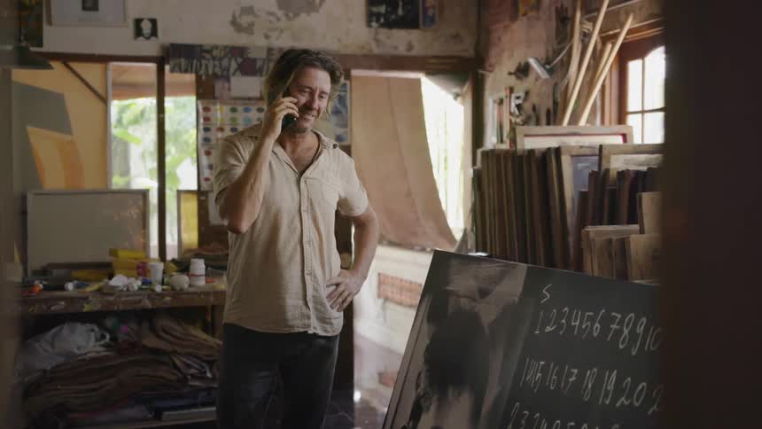 A man standing in an art studio talks on a phone