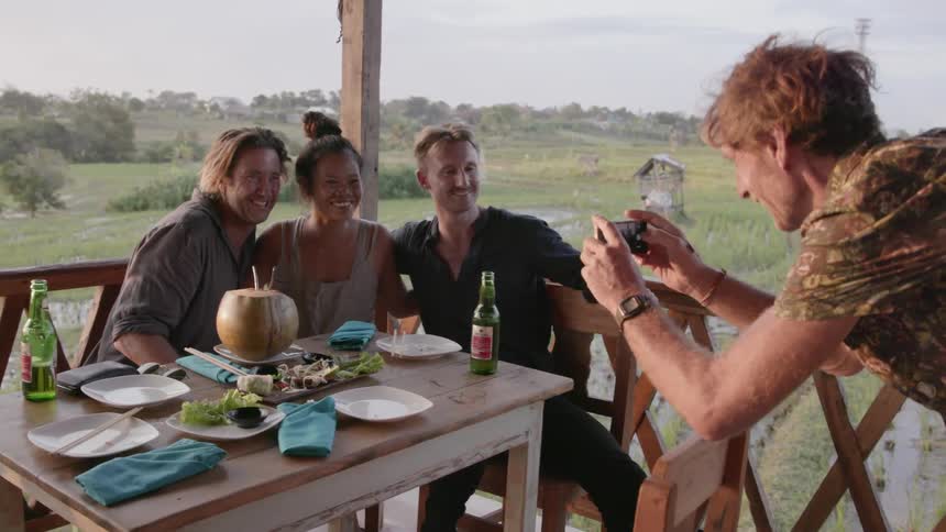 A man is taking a photo of friends at a restaurant table in daylight