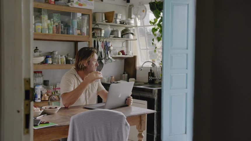 Man drinks from a mug as he holds a laptop and looks out the window