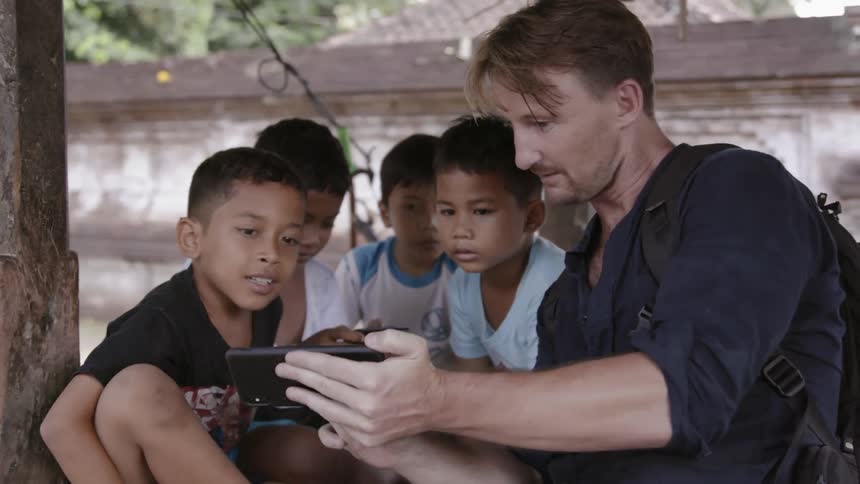 A man shows his phone to young kids