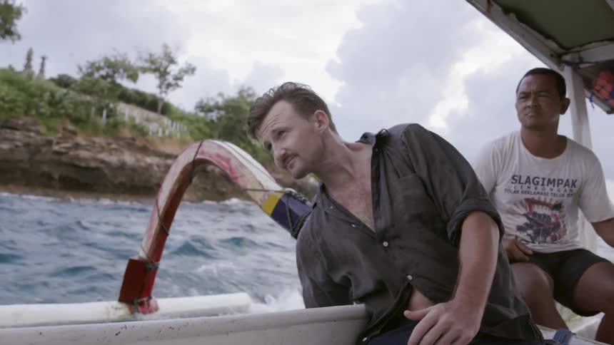 A man reaches into the water from a moving boat