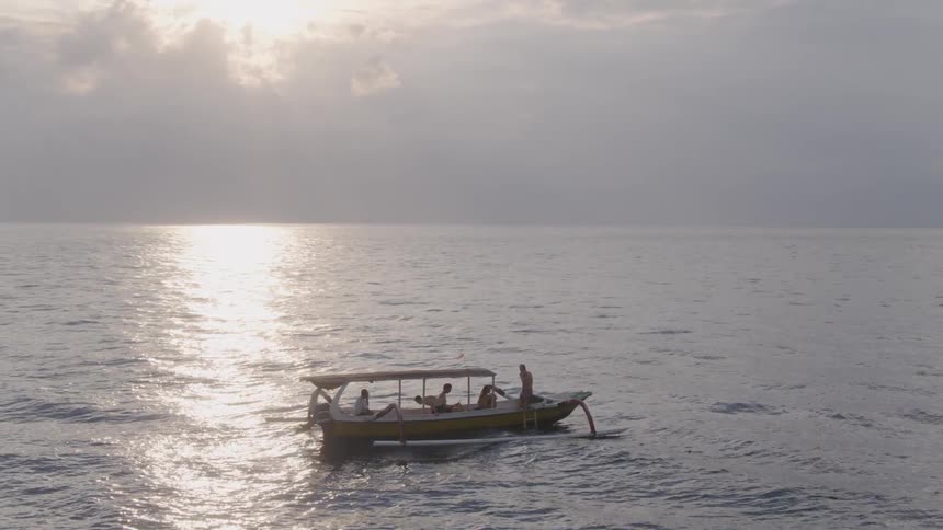 People sit and stand on a boat floating in the ocean at sunset